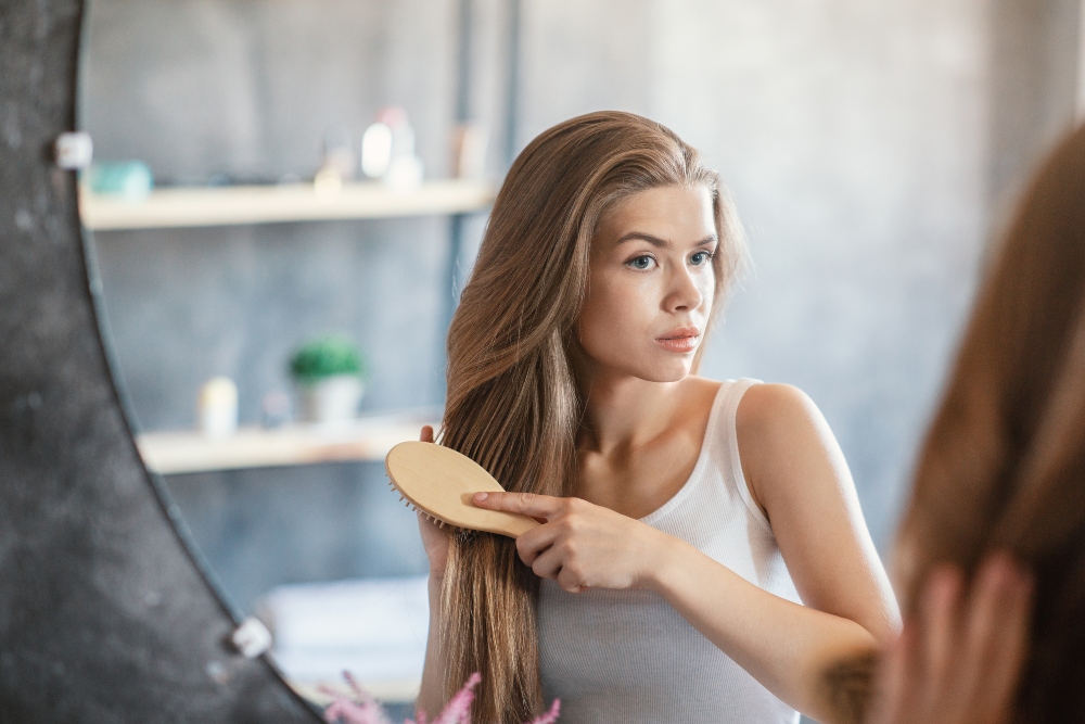 Lovely lady brushing her long beautiful hair in front of mirror at bathroom