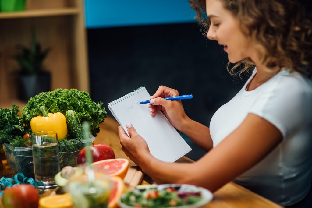 Nutritionist working in office. Doctor writing diet plan on table and using vegetables. Sport trainer.